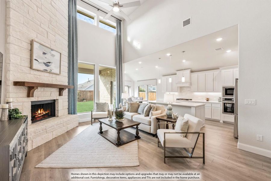 Open-concept living room with stone fireplace, vaulted ceiling, and kitchen visible in background