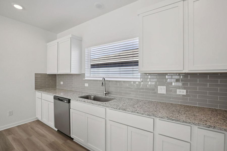 Kitchen with white cabinetry, light stone counters, light wood-style flooring, dishwasher, and decorative backsplash