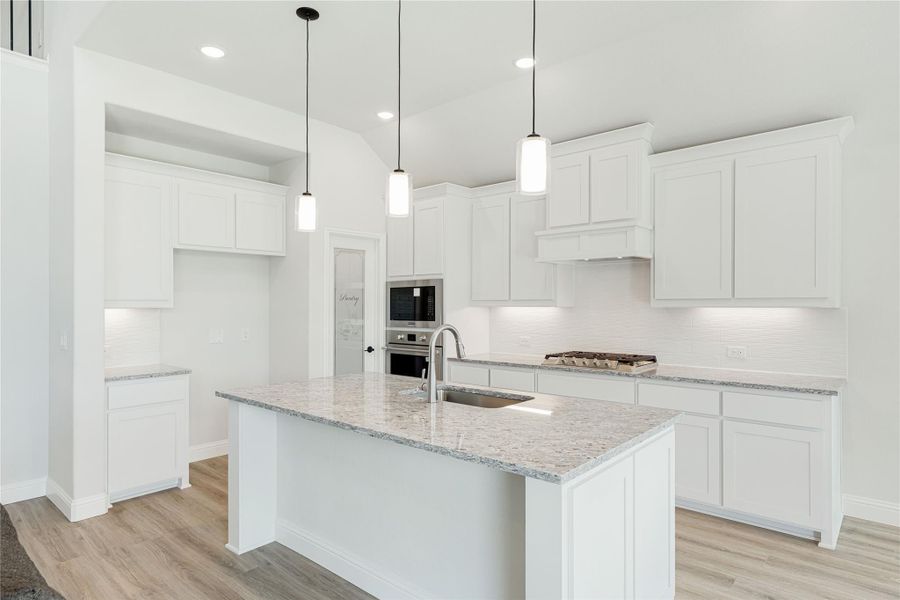White kitchen with granite island, pendant lights, stainless steel appliances, and light wood floors