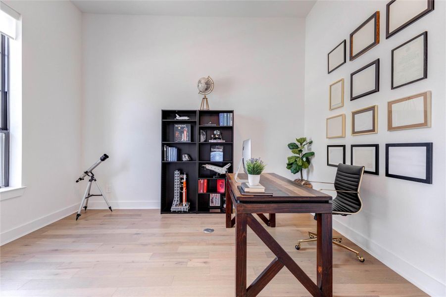 Modern home office with a sleek wooden desk, stylish chair, and a black bookshelf. Decor includes a telescope by the window, a plant, and a wall display of empty picture frames. The room features light wood flooring and ample natural light. Modern home office with a sleek wooden desk, stylish chair, and a black bookshelf. Decor includes a telescope by the window, a plant, and a wall display of empty picture frames. The room features light wood flooring and ample natural light.