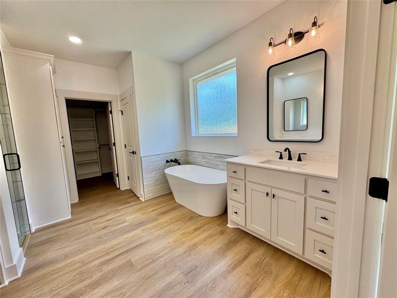 Full bathroom with vanity, light wood finished floors, a walk in closet, a freestanding tub, and tile walls