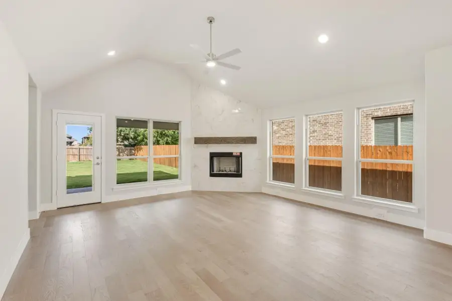 Open living room with vaulted ceiling, stone fireplace, ceiling fan, and light hardwood floors