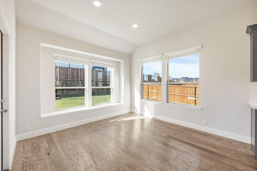 Empty room with light wood floors, white walls, and large windows overlooking a fenced backyard Empty room with light wood floors, white walls, and large windows overlooking a fenced backyard