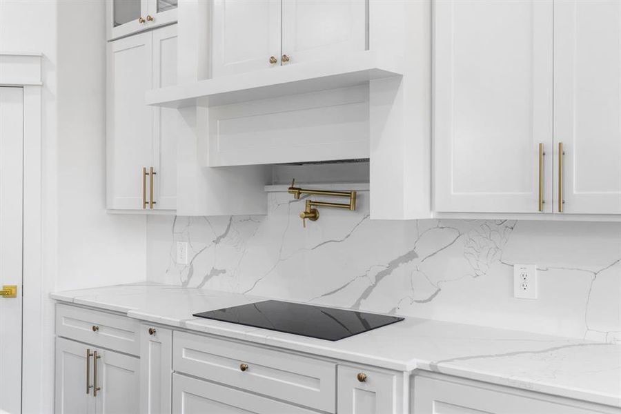 Kitchen featuring white cabinets, decorative backsplash, black electric stovetop, and light stone countertops