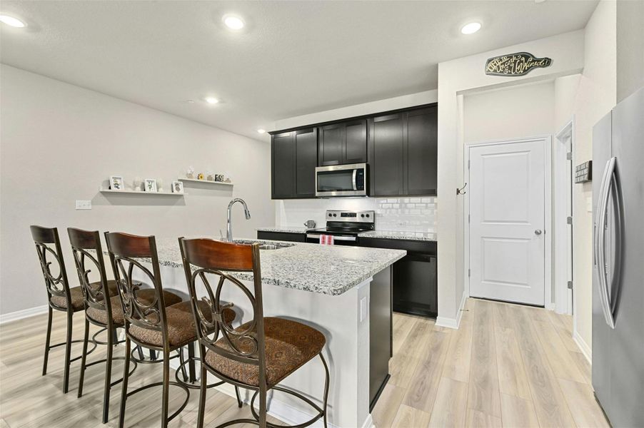 Kitchen featuring a kitchen breakfast bar, appliances with stainless steel finishes, sink, light stone countertops, and a center island with sink