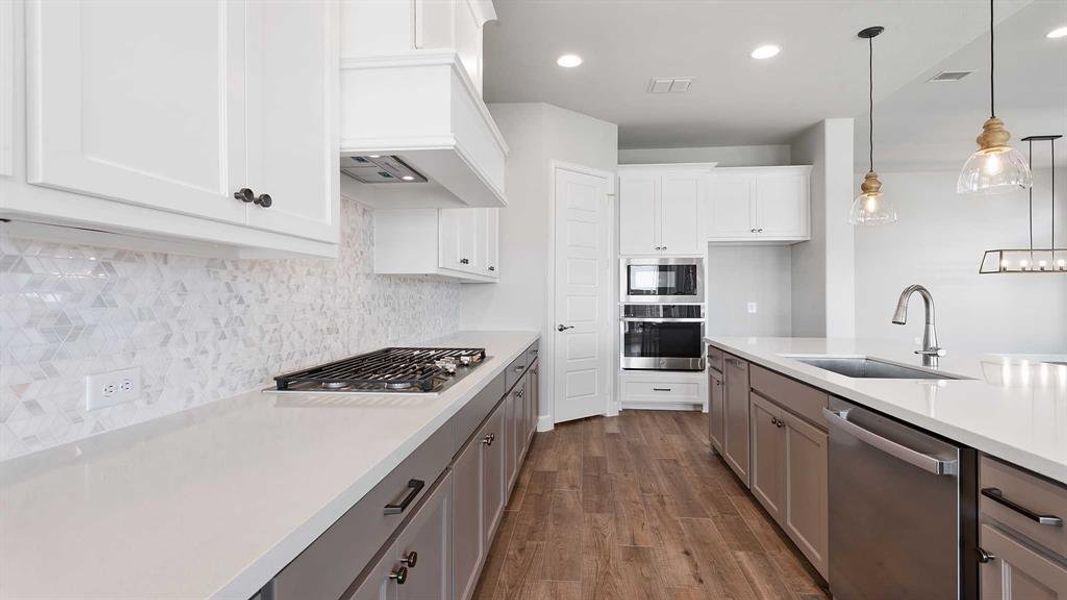 Kitchen with hardwood / wood-style floors, appliances with stainless steel finishes, white cabinetry, pendant lighting, and sink