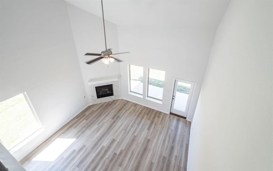 Unfurnished living room featuring a fireplace, high vaulted ceiling, light wood-type flooring, and ceiling fan