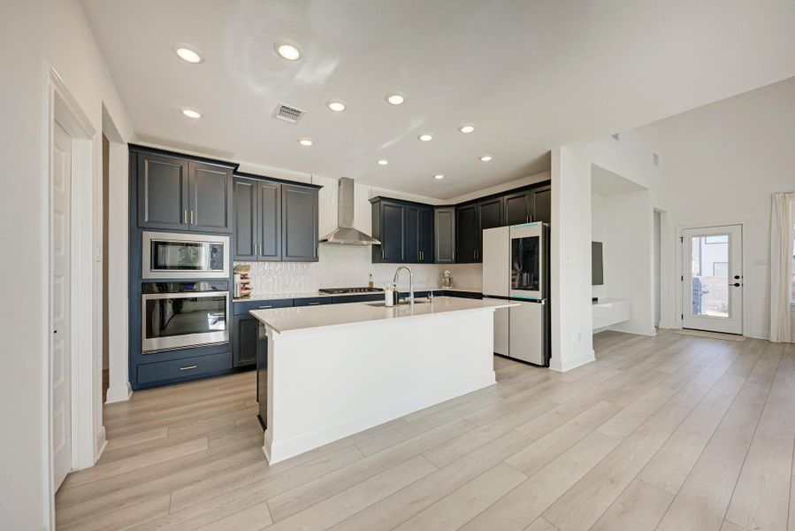 Kitchen featuring appliances with stainless steel finishes, a kitchen island with sink, wall chimney exhaust hood, recessed lighting, and light wood-style flooring