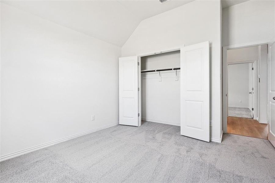 Unfurnished bedroom featuring light colored carpet, a closet, and high vaulted ceiling