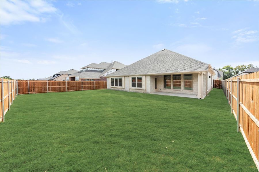 Backyard of a brick home with large green lawn, covered patio, and wood privacy fence on both sides.