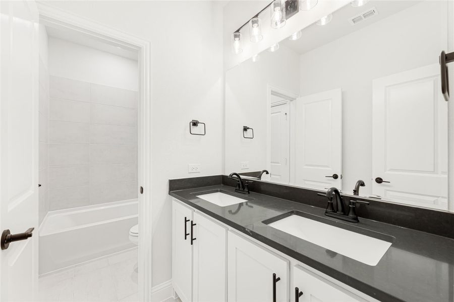 Bathroom with double sink vanity, dark countertops, white cabinets, and tiled tub-shower combo