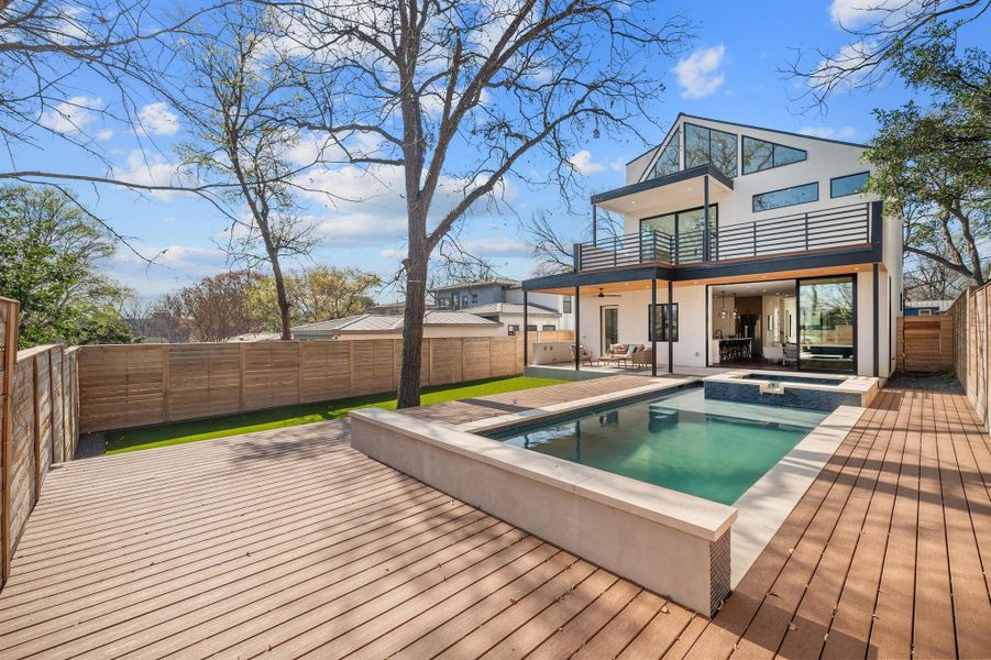 Back of house featuring a pool with connected hot tub, stucco siding, a fenced backyard, a balcony, and a patio