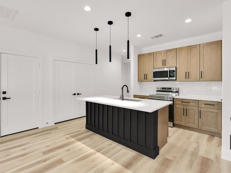 Kitchen with pendant lighting, electric range, sink, light hardwood / wood-style floors, and a kitchen island with sink