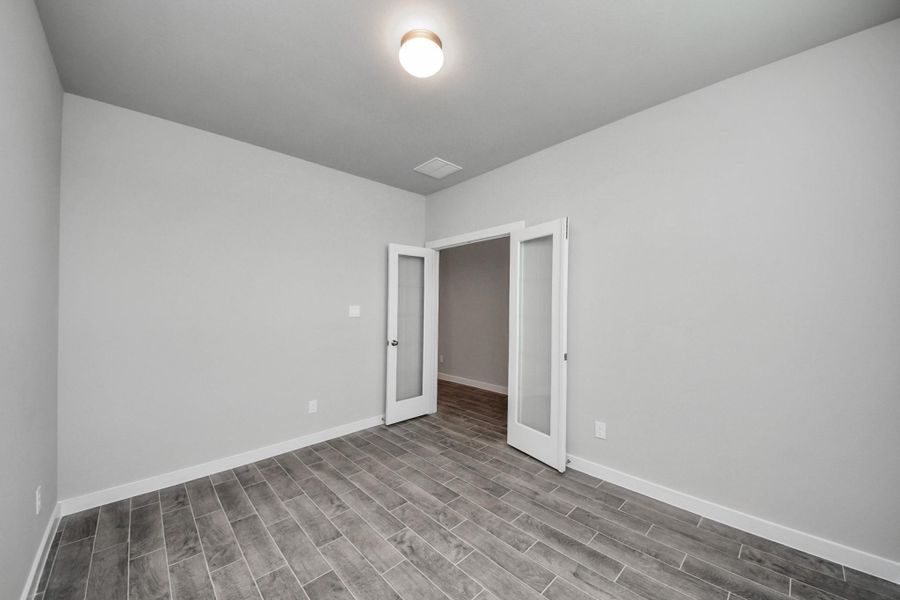 Experience the perfect blend of sophistication and warmth in this home office, boasting elegant wood-look tile flooring and flooded with natural light from expansive windows and French doors. Sample photo of completed home with similar floor plan. Actual colors and selections may vary.