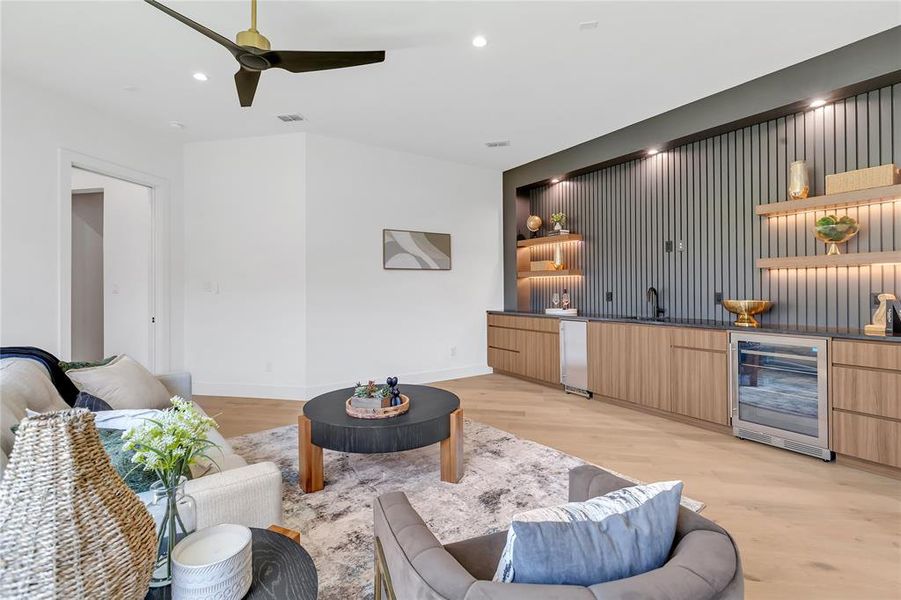 Living area featuring beverage cooler, bar with sink, light wood-type flooring, ceiling fan, and recessed lighting Living area featuring beverage cooler, bar with sink, light wood-type flooring, ceiling fan, and recessed lighting