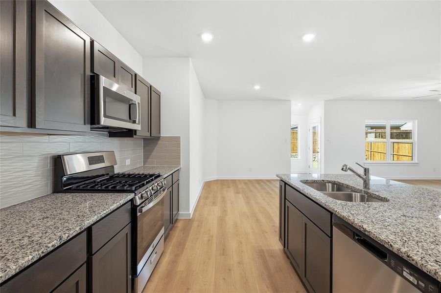 Kitchen featuring stainless steel appliances, light wood finished floors, light stone counters, dark wood finish cabinets, and recessed lighting