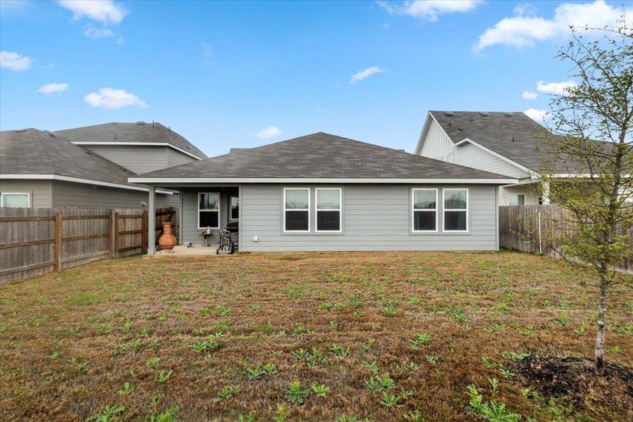 Rear view of house featuring a patio area, a fenced backyard, and a shingled roof