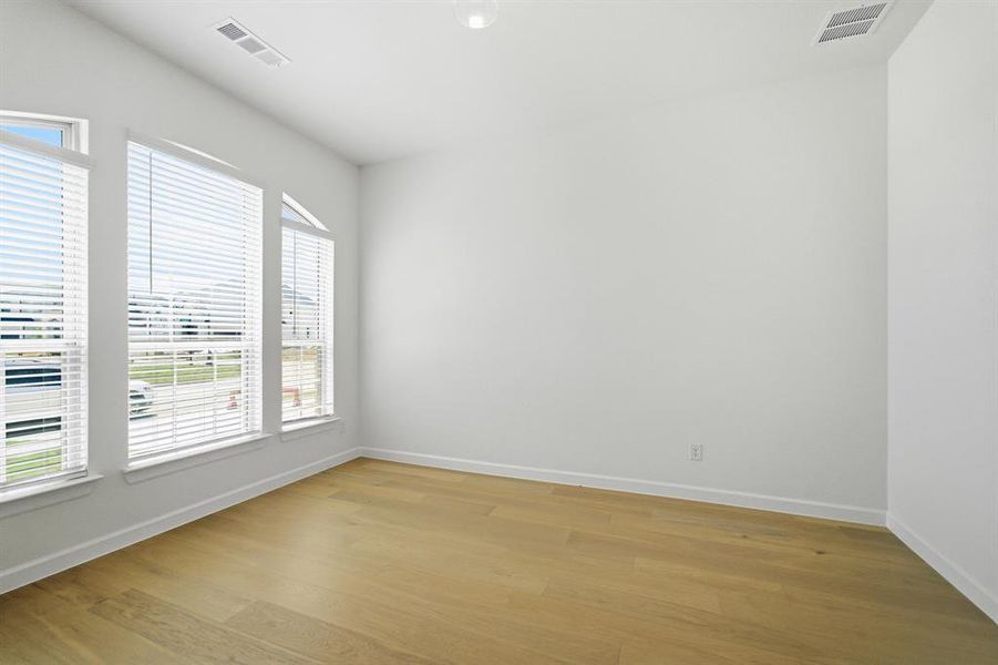 Spacious room featuring multiple large windows with horizontal blinds, light wood-finish flooring, white baseboards, and a neutral wall color