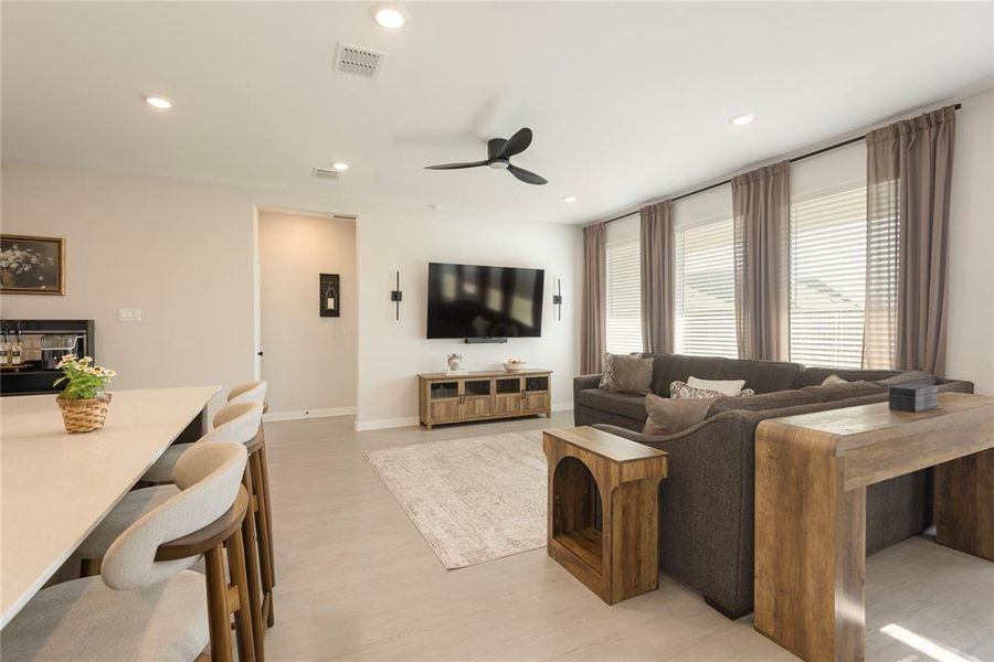 Spacious living area featuring light wood-finish flooring, recessed lighting, and a modern ceiling fan Spacious living area featuring light wood-finish flooring, recessed lighting, and a modern ceiling fan