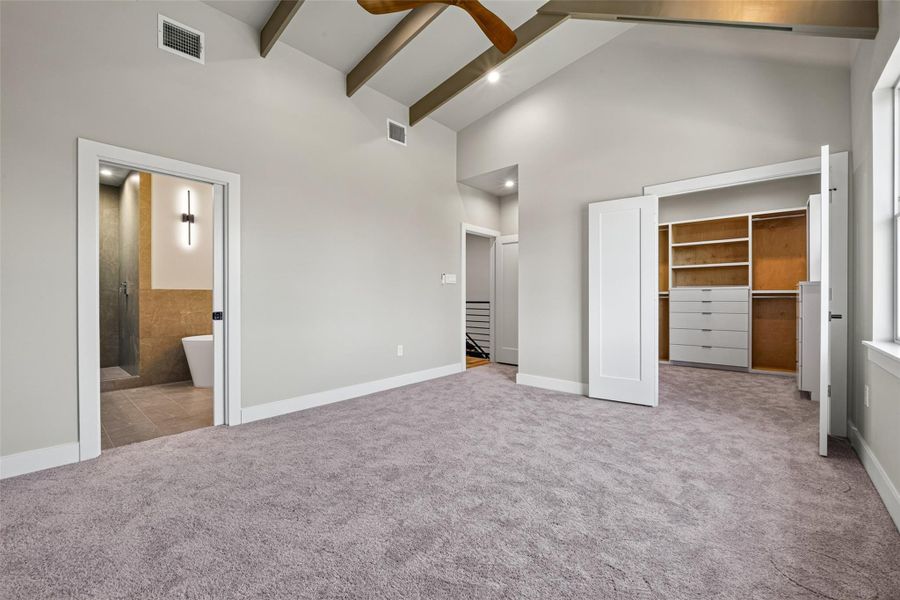The primary suite occupies the top floor and impresses immediately with its vaulted ceiling featuring exposed decorative wood beams, large windows on two elevations, and plush carpet. A ceiling fan and generous walk-in closet make this a true owner's retreat.
