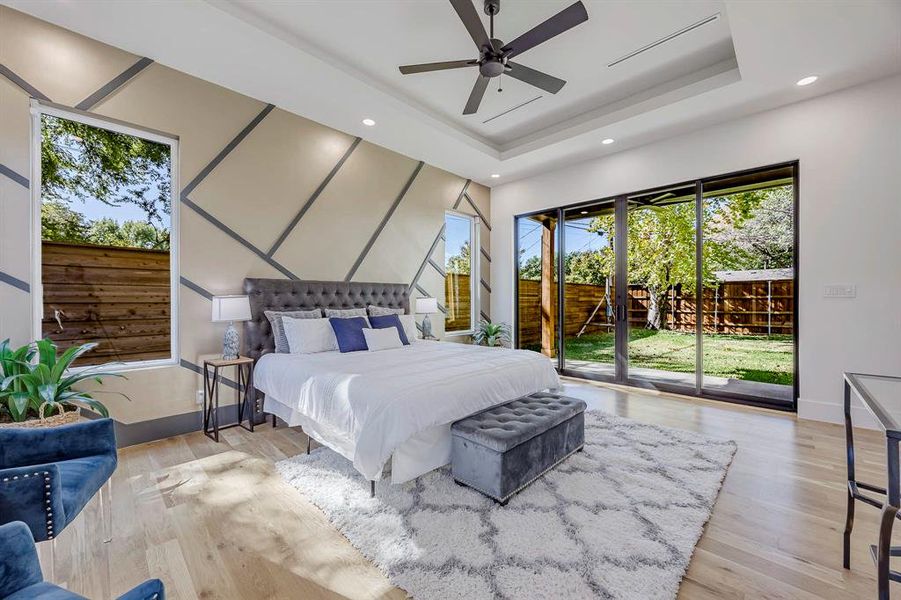 Bedroom featuring access to exterior, light wood-style floors, ceiling fan, a raised ceiling, and recessed lighting Bedroom featuring access to exterior, light wood-style floors, ceiling fan, a raised ceiling, and recessed lighting