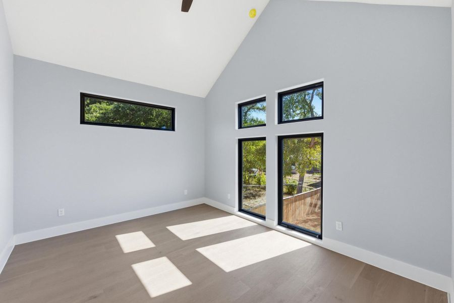 Empty room featuring high vaulted ceiling, wood finished floors, healthy amount of natural light, and ceiling fan Empty room featuring high vaulted ceiling, wood finished floors, healthy amount of natural light, and ceiling fan