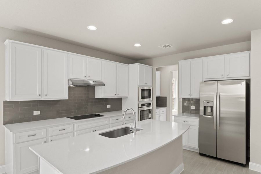 A Kitchen with white countertops, white cabinets, steel appliances, and gray blacksplash tile, white painted walls and vinyl flooring.