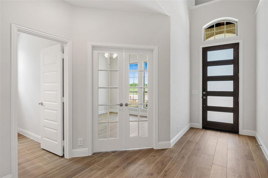 Foyer featuring french doors, plenty of natural light, light wood finished floors, and a towering ceiling