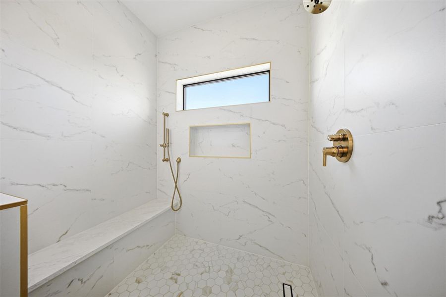 Same floorplan - different finishes. The walk-in shower is finished with marble-patterned wall tiles, a recessed storage niche with gold trim, and a built-in bench.