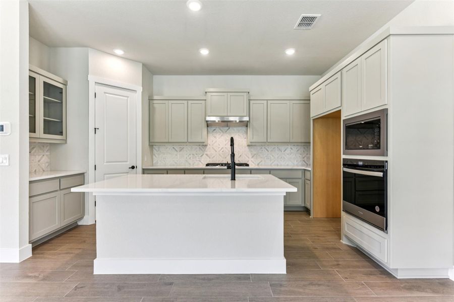 Kitchen with backsplash, a kitchen island with sink, stainless steel appliances, wood tiled floors, and recessed lighting Kitchen with backsplash, a kitchen island with sink, stainless steel appliances, wood tiled floors, and recessed lighting
