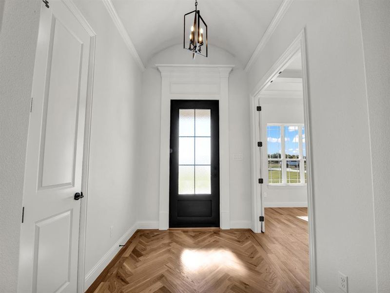 Entryway with crown molding, light parquet floors, lofted ceiling, and an inviting chandelier