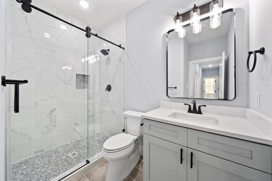 Bathroom featuring a glass-enclosed shower with large format white tile, a mosaic tile shower floor, and matte black fixtures