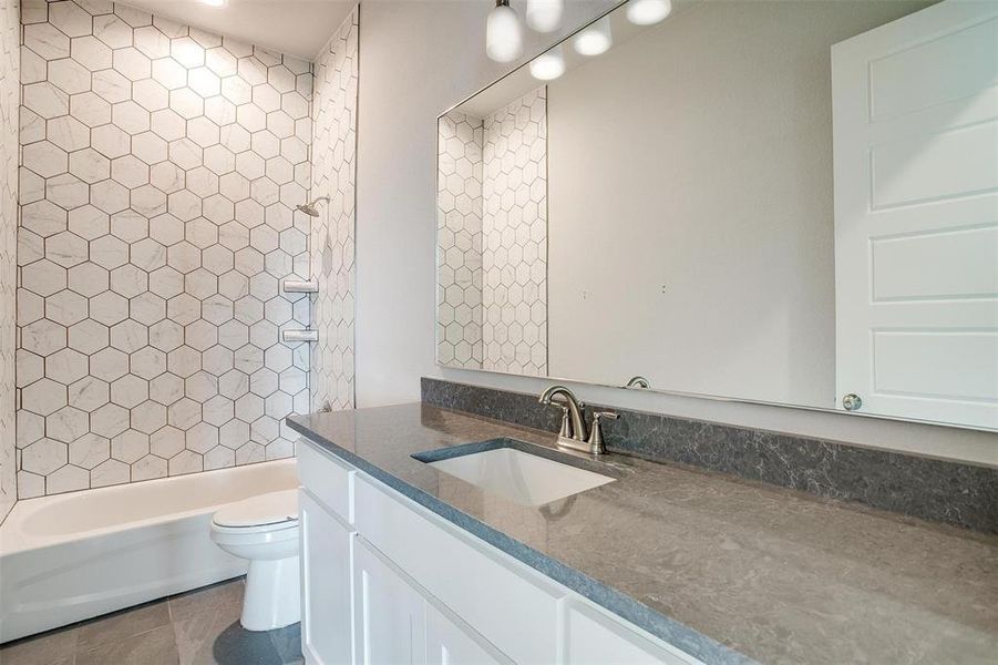 Full bathroom with tile floors, tiled shower / bath combo, oversized vanity, and toilet