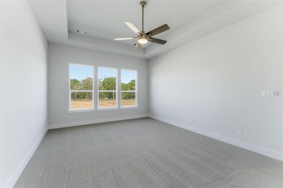 Empty room with light colored carpet, a ceiling fan, and a tray ceiling