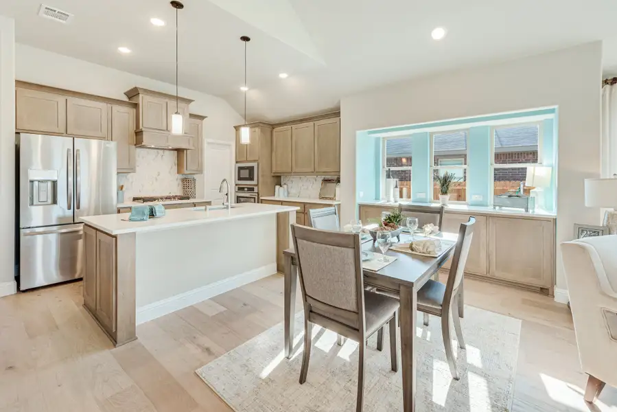 Open kitchen and dining area with tan cabinets, center island, stainless appliances, and light hardwood floors