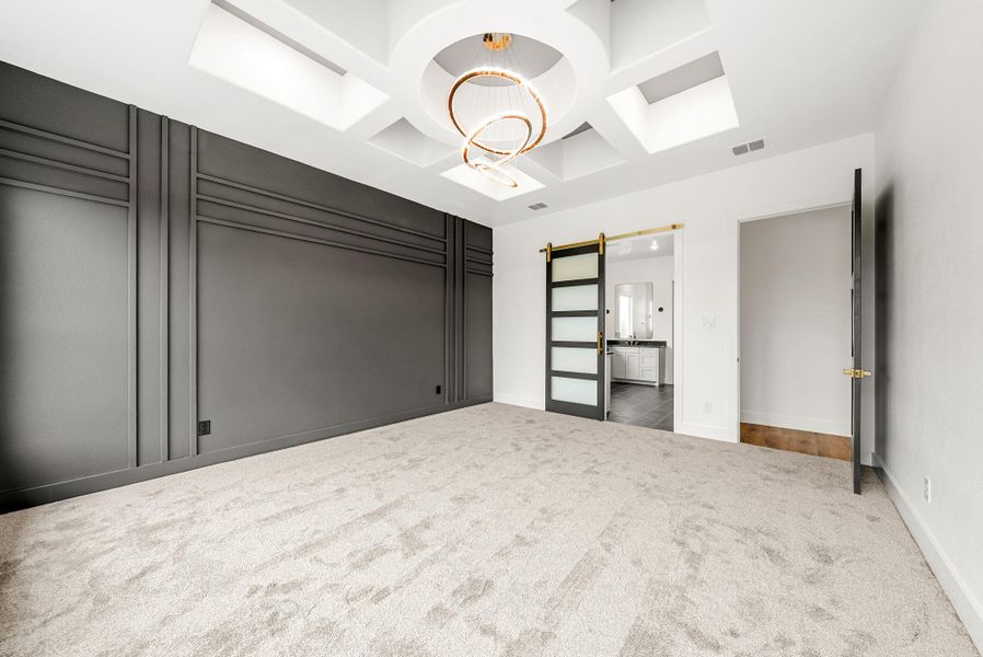 Ornate ceiling design with a modern chandelier illuminates this spacious room, featuring a sleek accent wall and plush carpeting.