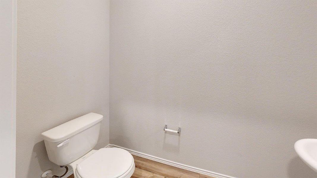 Restroom featuring a white toilet, wood-finish flooring, white baseboards, and a wall-mounted toilet paper holder Restroom featuring a white toilet, wood-finish flooring, white baseboards, and a wall-mounted toilet paper holder