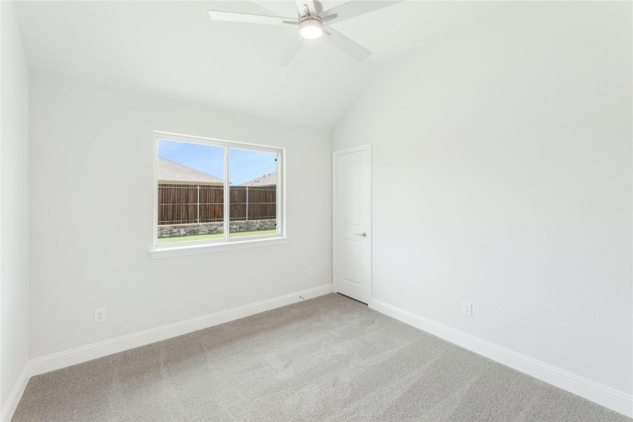 Empty bedroom with vaulted ceiling, ceiling fan, carpet flooring, and backyard-facing window Empty bedroom with vaulted ceiling, ceiling fan, carpet flooring, and backyard-facing window
