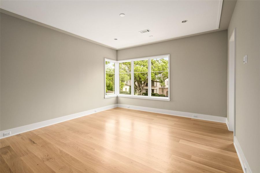 Generously sized secondary bedroom featuring a unique corner window with tree-lined street views, complete with a large walk-in closet and ensuite bath.