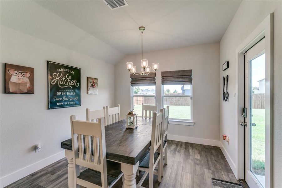 Dining space featuring a chandelier, vaulted ceiling, dark hardwood / wood-style flooring, and a healthy amount of sunlight