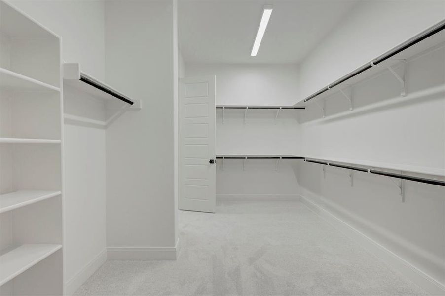 Spacious walk-in closet featuring extensive built-in shelving, multiple hanging rods, clean white walls, light gray carpeting, and recessed ceiling lighting Spacious walk-in closet featuring extensive built-in shelving, multiple hanging rods, clean white walls, light gray carpeting, and recessed ceiling lighting