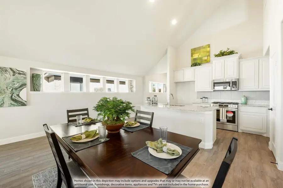 Open dining area with dark wood table and kitchen featuring white cabinets and stainless appliances under vaulted ceiling