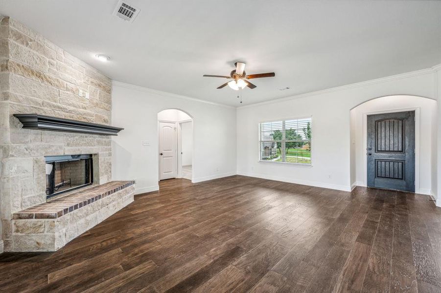 Unfurnished living room featuring ceiling fan, dark hardwood / wood-style floors, a fireplace, and ornamental molding