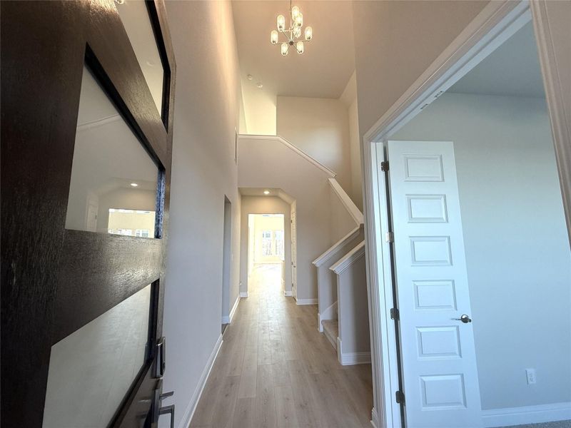 Entryway with light wood finished floors, a chandelier, stairs, and a towering ceiling