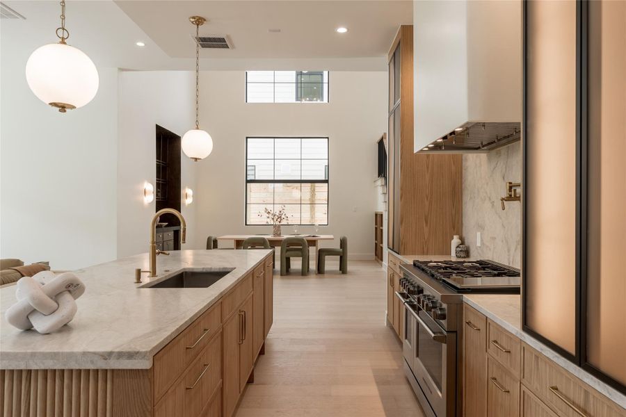 Integrated cabinet lighting highlights the custom white oak cabinetry and sculptural hood, while the kitchen’s open exposure to the soaring dining room creates a striking visual connection between the two spaces. Integrated cabinet lighting highlights the custom white oak cabinetry and sculptural hood, while the kitchen’s open exposure to the soaring dining room creates a striking visual connection between the two spaces.