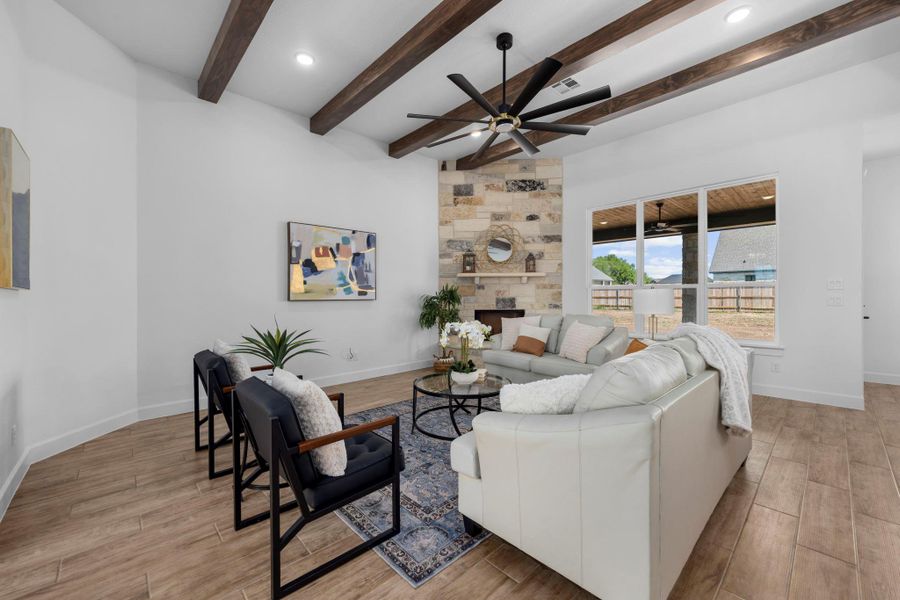 Living room with wood finish floors, ceiling fan, a stone fireplace, recessed lighting, and beamed ceiling
