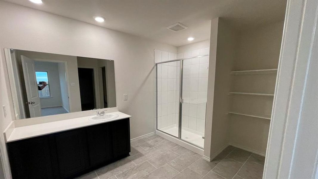 Bathroom featuring a dark wood-finish vanity with a white countertop and integrated sink, a large wall-mounted mirror, a glass-enclosed shower with white tiled walls, and recessed lighting