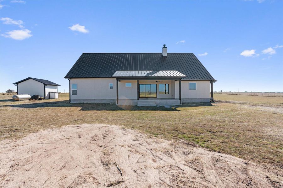 Rear view of property with a metal roof, a patio, an outbuilding, a yard, and a chimney