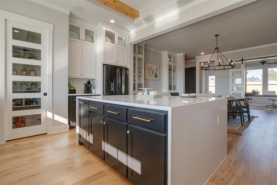 Kitchen with stainless steel refrigerator with ice dispenser, beamed ceiling, white cabinets, a kitchen island, and hanging light fixtures