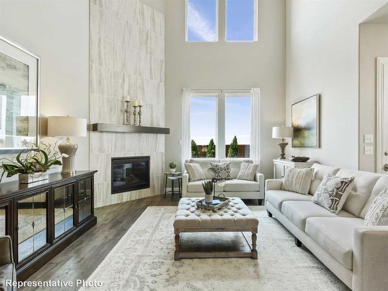 Two-story living area featuring a full-height tiled fireplace with a dark wood mantel, high vaulted ceilings, and a series of tall windows providing ample natural light